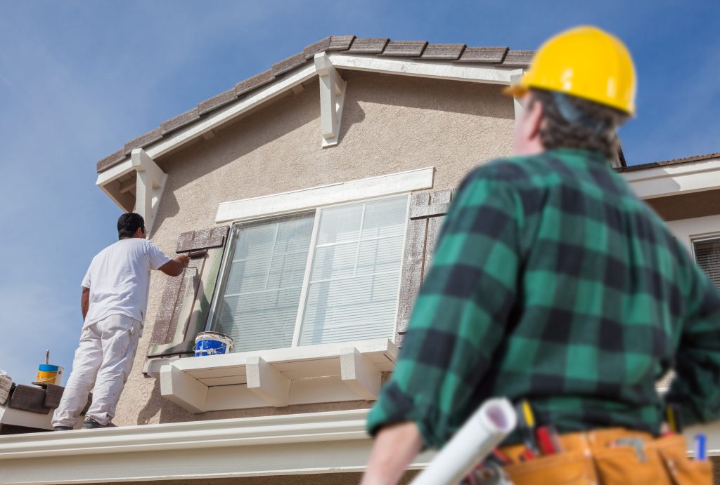 Painting crew working on a house exterior with a contractor overseeing the job